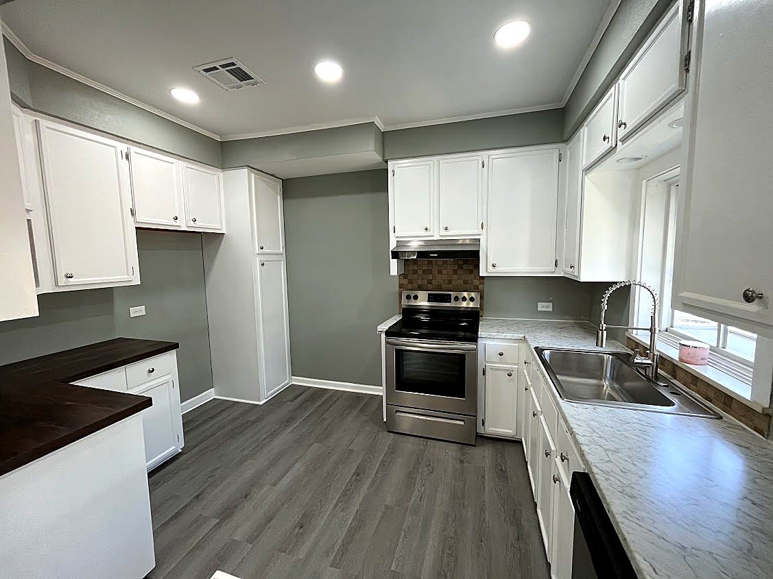 Kitchen after the remodel: white cabinets, stainless range, new counters and gray floors
